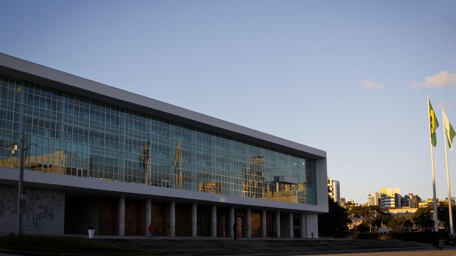 Palácio Iguaçu, no Centro Cívico de Curitiba, com a longa fachada de vidro, colunas no térreo e as bandeiras do Brasil e do Paraná