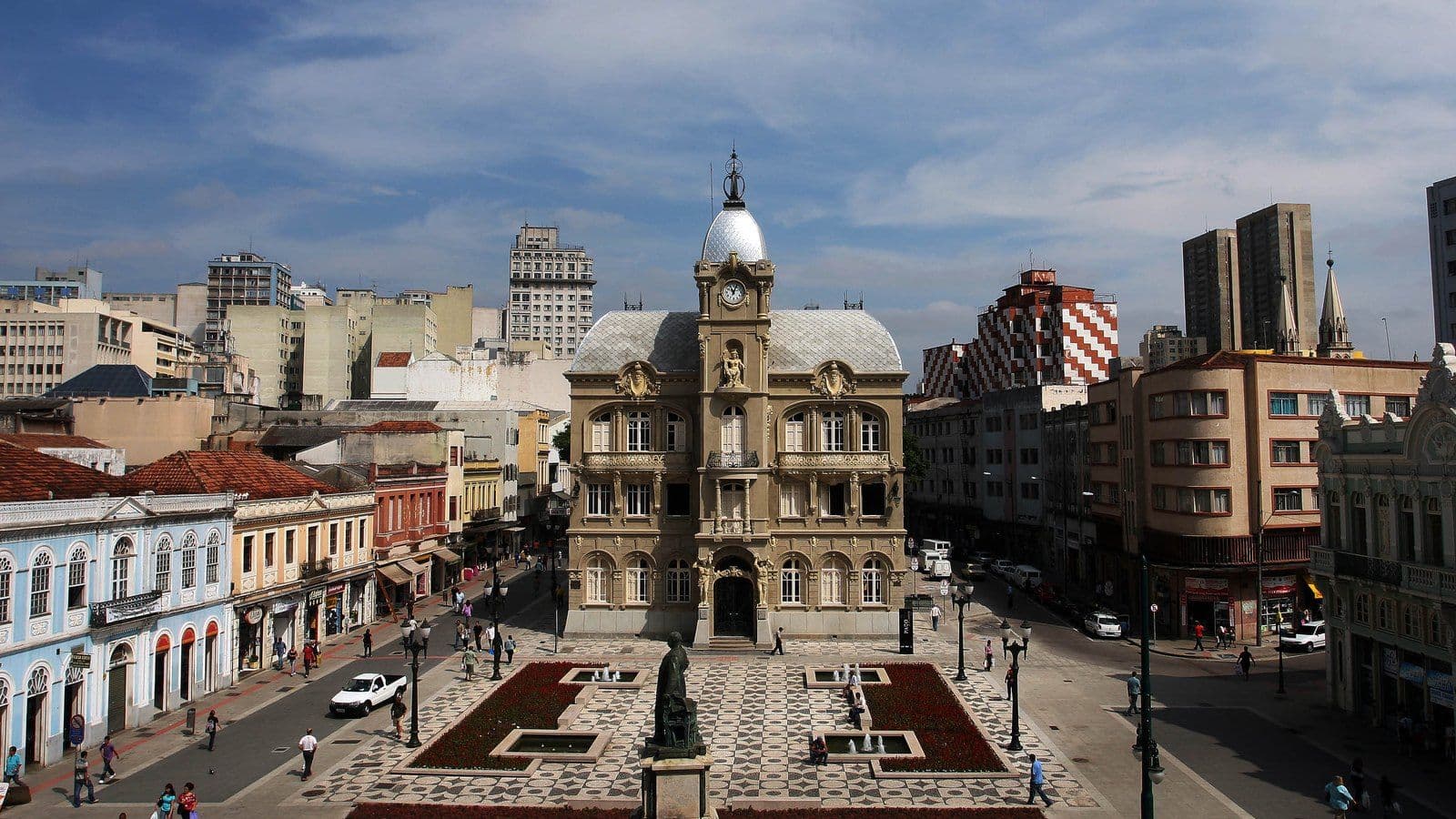 Paço da Liberdade visto do alto, em Curitiba, com a Praça Generoso Marques em frente: calçada de mosaico, canteiros floridos e fontes
