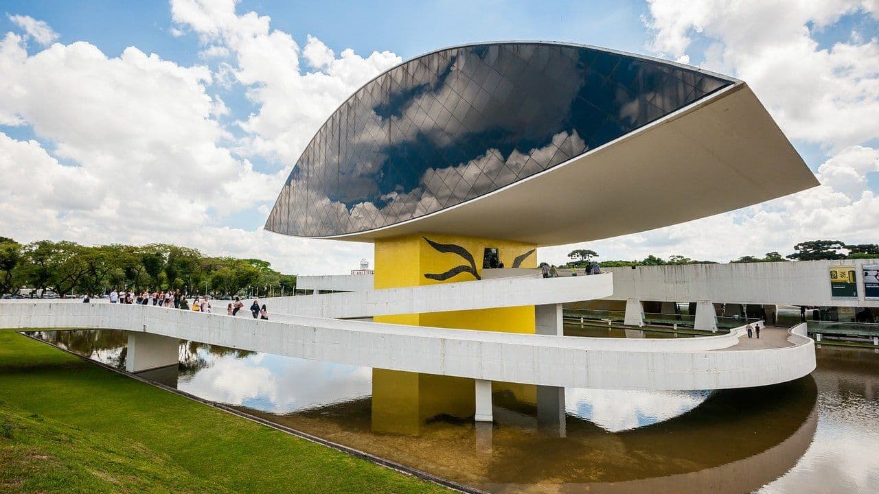 Museu Oscar Niemeyer, em Curitiba: o anexo em forma de olho, de vidro escuro, sobre um pilar amarelo, com rampas brancas e espelho d'água