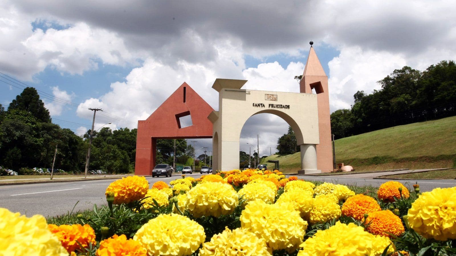 Portal de Santa Felicidade, em Curitiba, com arco, torre e o nome do bairro, atrás de um canteiro de flores amarelas e laranja